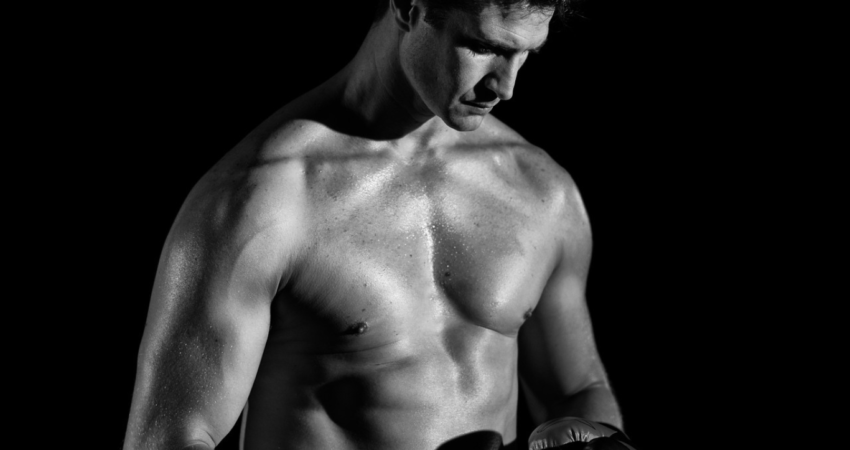 Mustavalkoinen kuva lihaksikkaasta miehestä nyrkkeilyhanskat kädessä