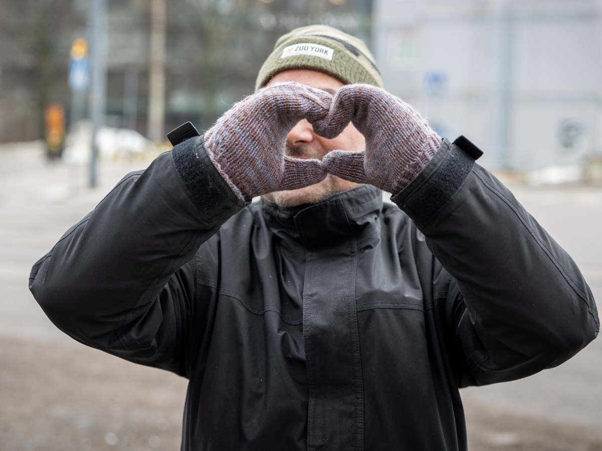 Henkilö seisoo ulkona talvisessa ympäristössä, pukeutuneena mustaan takkiin, harmaisiin lapasiin ja vihreään pipoon, jossa lukee "New York". Hän muodostaa käsillään sydämenmuotoisen eleen kasvojensa eteen.